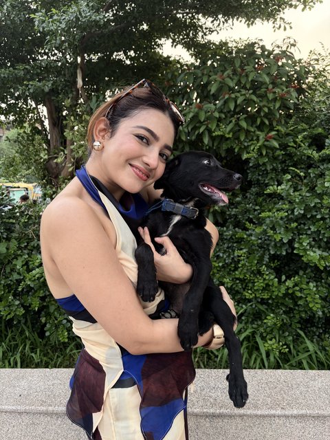 Shrestha Dutta cuddling a rescued black puppy, lying in the grass