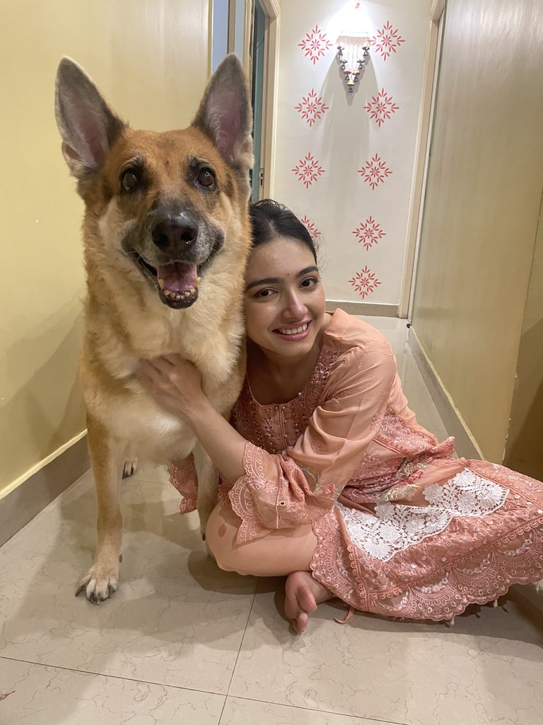 Shrestha Dutta sitting on the floor with her arm around a large German Shepherd, a candid moment at home