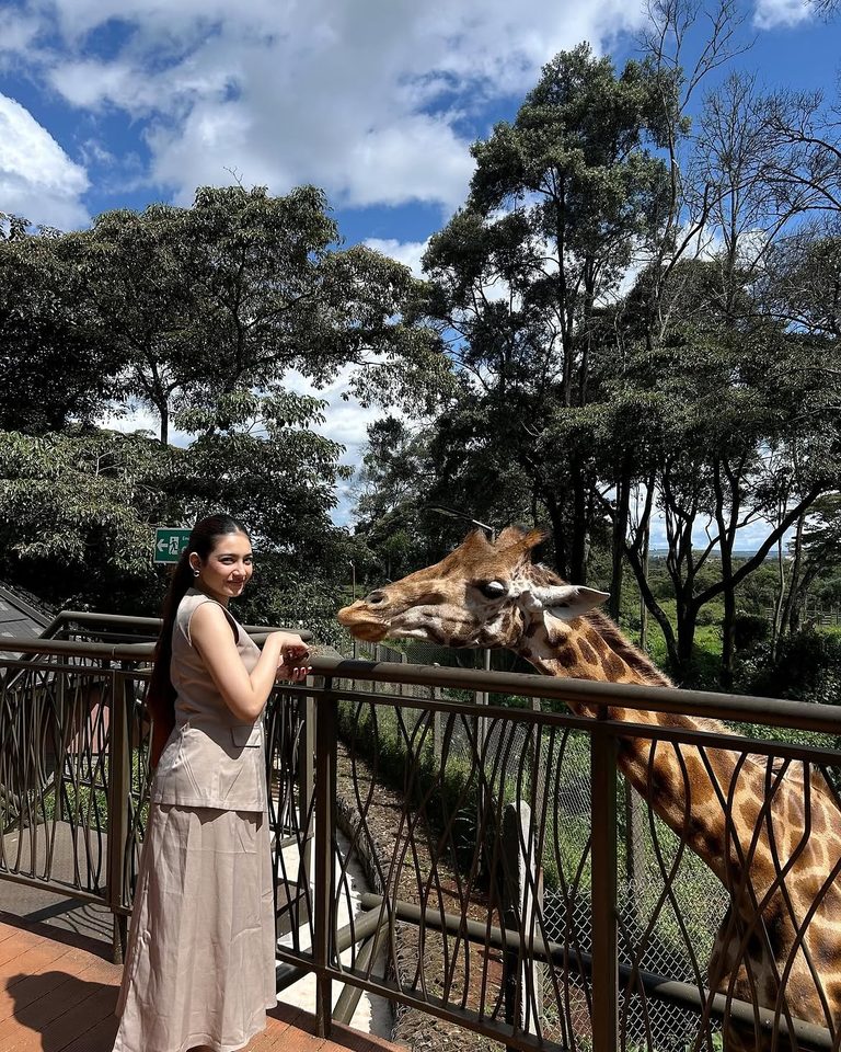 Shrestha Dutta reaching toward a giraffe from a safari walkway in Kenya